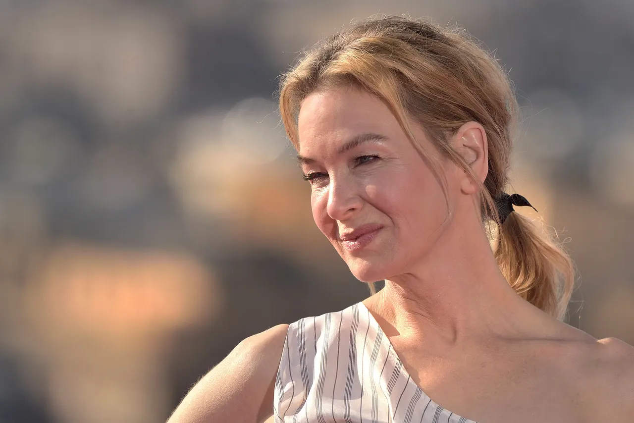 Renée Zellweger trägt ein einen Zopf und wird lächelnd von der Seite abgelichtet. 