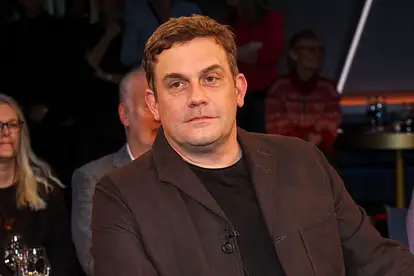 Sebastian Bezzel sitzt und schaut ernst in die Ferne.