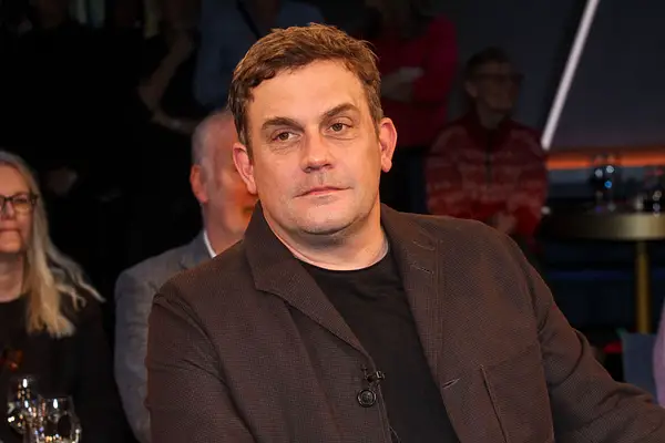 Sebastian Bezzel sitzt und schaut ernst in die Ferne.