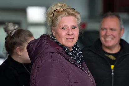 Silvia Wollny steht im Vordergrund und schaut in die Kamera. Sie trägt eine Lila-farbene Winterjacke. Im Hintergrund erkennt man unscharf ihren Lebensgefährten Harald Elsenbast. 