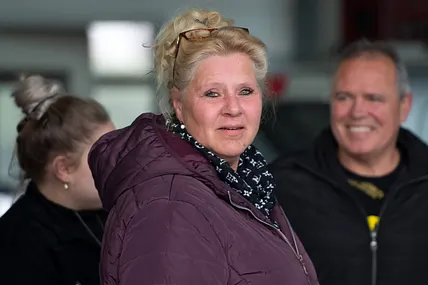 Silvia Wollny steht im Vordergrund und schaut in die Kamera. Sie trägt eine Lila-farbene Winterjacke. Im Hintergrund erkennt man unscharf ihren Lebensgefährten Harald Elsenbast. 