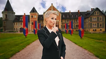 Sonja Zietlow steht vor einem Anwesen und hält sich einen Finger vor die Lippen.