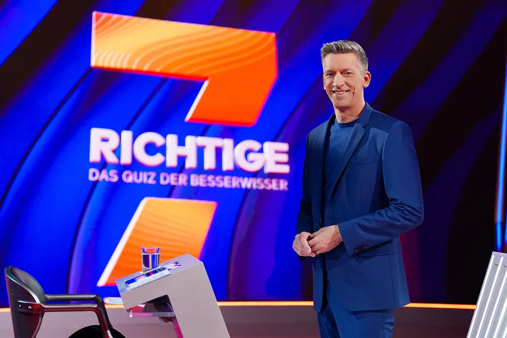 Steffen Hallaschka posiert lächelnd vor dem Logo seiner neuen Quizshow "7 Richtige". Steffen Hallaschka posiert lächelnd vor dem Logo seiner neuen Quizshow "7 Richtige".