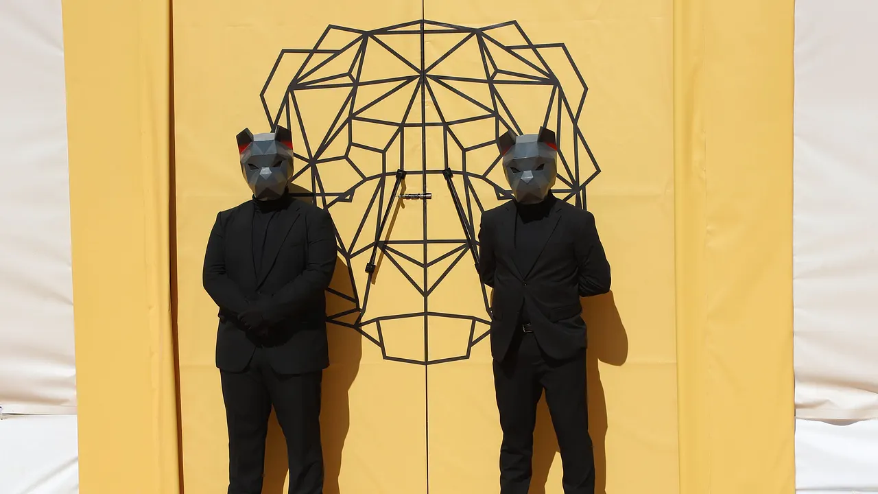The 50: Die Löwen sorgen für Ordnung Zwei Personen in schwarzer Kleidung und mit schwarzen Löwenmasken stehen vor zwei gelben Türen, auf denen ein stilisierter Löwenkopf zu sehen ist. - Foto: Prime Video