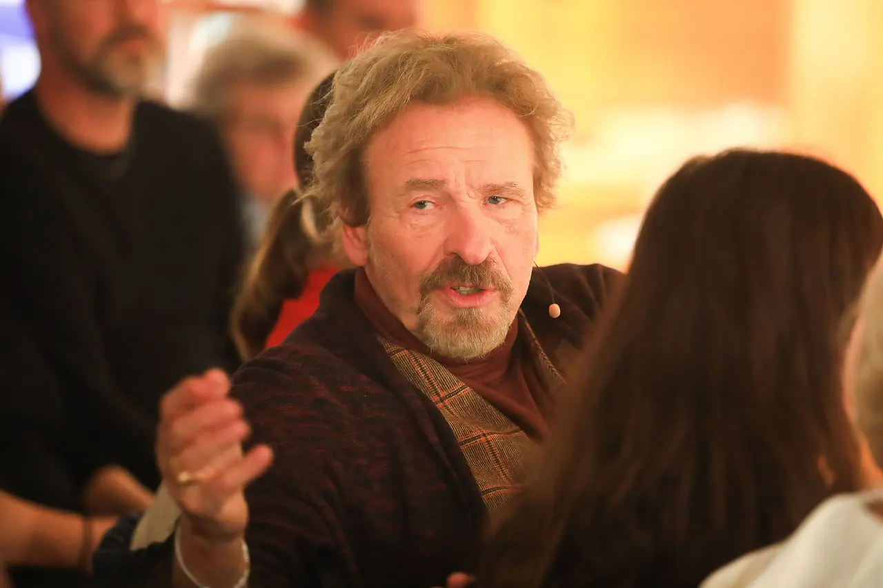 Thomas Gottschalk sitzt an einem Tisch und gestikuliert mit der rechten Hand.