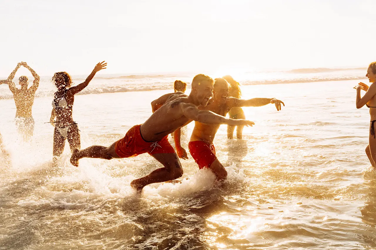 THTH_S2_Unit_©PaulHepper_Netflix_076 Mehrere Männer und Frauen tummeln sich bei Sonnenuntergang im seichten Wasser am Strand. - Foto: Paul Hepper / Netflix
