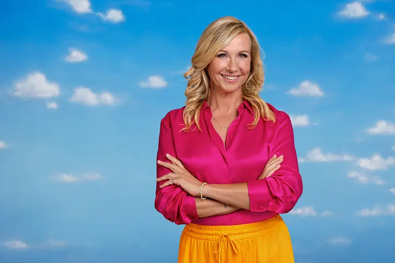 Andrea Kiewel lächelt mit verschränkten Armen in die Kamera. Hinter ihr ist ein blauer Himmel mit kleinen, weißen Wolken zu sehen.