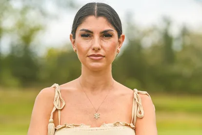 Yeliz Koc steht vor einem grünen Hintergrund mit geradem Blick in die Kamera und verschränkten Armen.