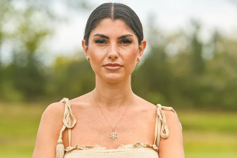 Yeliz Koc steht vor einem grünen Hintergrund mit geradem Blick in die Kamera und verschränkten Armen.